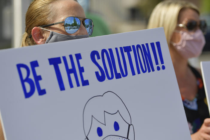 Demonstrators calling on people to wear masks gather outside school district headquarters in Marietta, Ga., last week. A recent review at pandemic data finds requiring masks, capping the size of gatherings and instituting certain bar, gym and restaurant restrictions are all strategies that can help stop a surge in COVID-19 hospitalizations.