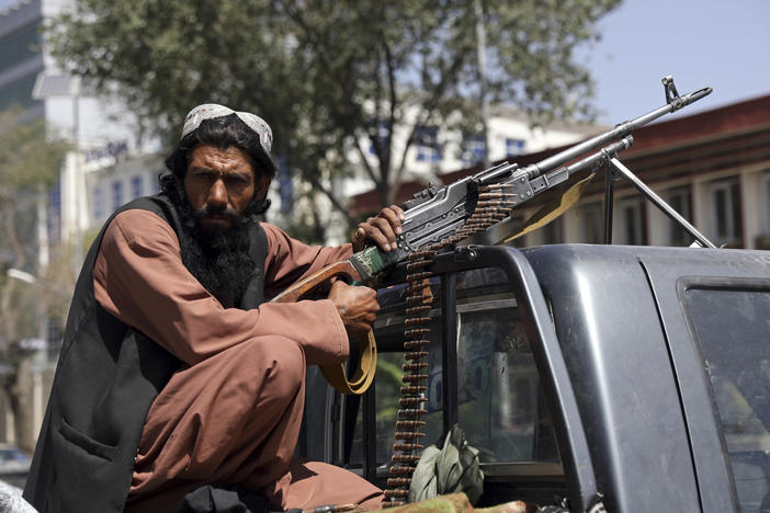 A Taliban fighter sits on the back of a vehicle with a machine gun in front of the main gate leading to the Afghan presidential palace, in Kabul, Afghanistan, Monday, Aug. 16, 2021. The U.S. military has taken over Afghanistan's airspace as it struggles to manage a chaotic evacuation after the Taliban rolled into the capital.