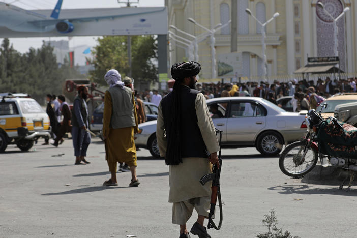 Taliban fighters stand guard in front of the Hamid Karzai International Airport in Kabul, Afghanistan, Monday. Thousands of people packed into the airport, rushing the tarmac and pushing onto planes in desperate attempts to flee the country after the Taliban took over.