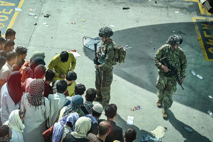 U.S. soldiers stand guard as Afghans wait Monday at the Kabul airport following the swift end to Afghanistan's 20-year war.