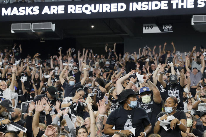 Raiders fans do the wave during last weekend's preseason game in Las Vegas as a stadium sign reminds them to wear face masks. The team now says spectators will have to show proof of vaccination — and that no masks will be required for those who have been vaccinated.