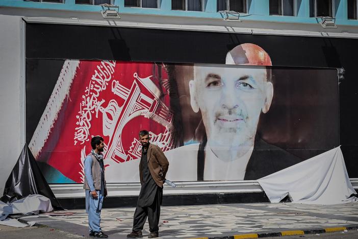 Men stand next to a torn poster of ousted Afghan President Ashraf Ghani at the Kabul airport on Monday. Ghani fled Afghanistan over the weekend as Taliban forces closed in on Kabul.