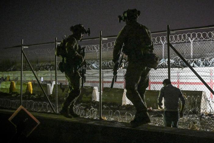 British and Canadian soldiers stand guard late Sunday near a canal as Afghans wait outside the foreign military-controlled part of the airport in Kabul, hoping to flee the country following the Taliban's military takeover of Afghanistan.