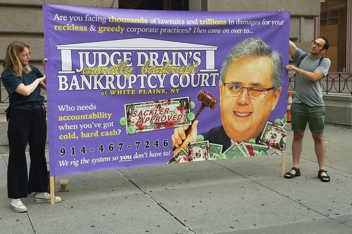 Two demonstrators protest against U.S. Judge Robert Drain, who has granted immunity from future opioid lawsuits to members of the Sackler family.