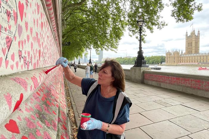 Fran Hall paints hearts on a memorial in London dedicated to people who have died from COVID-19. She and other activists are pushing for the British government to investigate its handling of the pandemic.