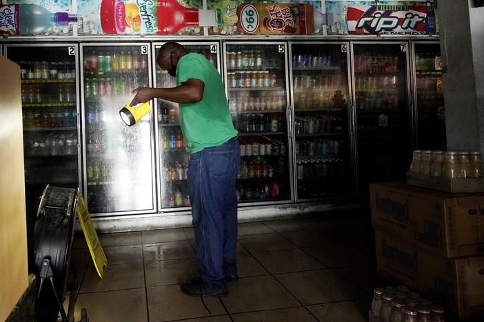 A man uses a flashlight to help others shop in the dark at a convenience store after the effects of Hurricane Ida knocked out power across New Orleans.