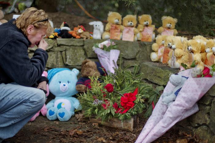 A mourner kneels beside 26 teddy bears, each representing a victim of the Sandy Hook Elementary School shooting, at a sidewalk memorial in 2012 in Newtown, Conn.