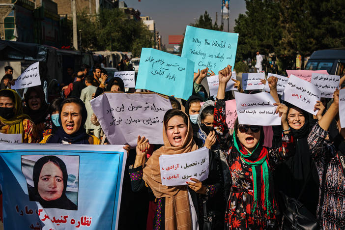 Protesters march in Kabul on Wednesday, a day after the Taliban announced their all-male interim government. At left, a protester carries a sign with a photo showing Banu Negar, a pregnant police officer who was killed in front of her relatives early this week in Ghor province. Family members accuse the Taliban of carrying out the killing.