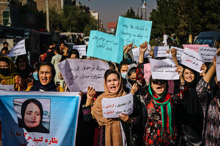 Protesters march in Kabul on Wednesday, a day after the Taliban announced their all-male interim government. At left, a protester carries a sign with a photo showing Banu Negar, a pregnant police officer who was killed in front of her relatives early this week in Ghor province. Family members accuse the Taliban of carrying out the killing.