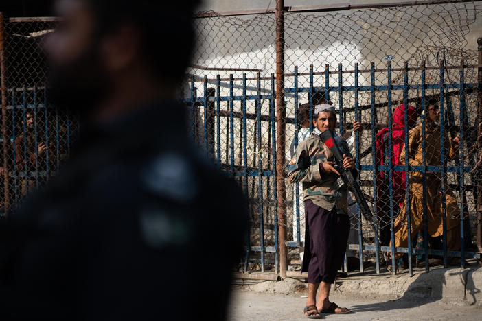 A Taliban guard stands on the Afghan side of the Torkham border crossing with Pakistan. People behind wait either to leave Afghanistan or to receive those returning to the country.