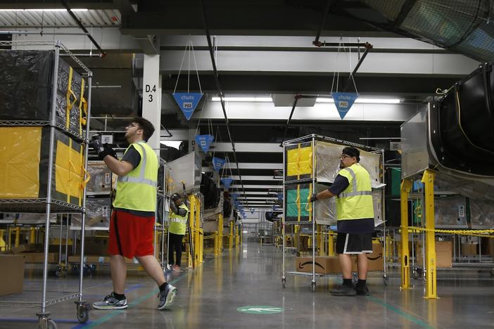 Amazon workers move containers to delivery trucks at an Amazon warehouse facility in Goodyear, Ariz., in December 2019.
