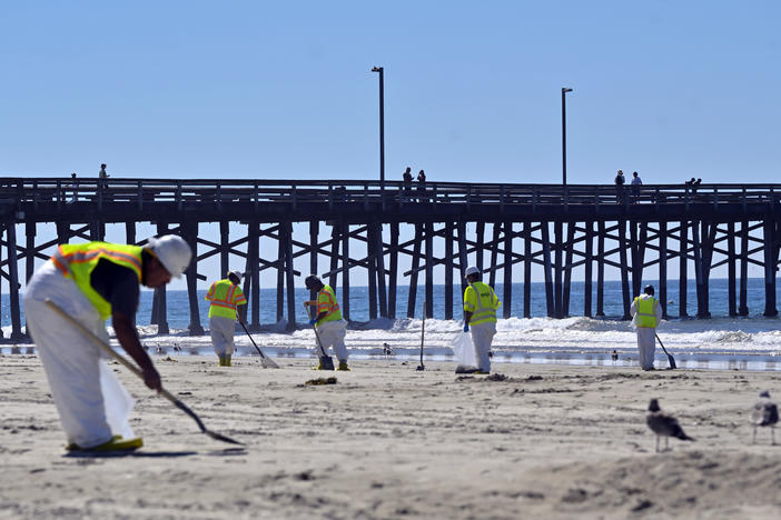 Workers clean oil from the sand, south of the pier, in Newport Beach, Calif., Tuesday, Oct. 5, 2021. A leak in an oil pipeline caused a spill off the coast of Southern California, sending about 126,000 gallons of oil into the ocean, some ending up on beaches in Orange County.