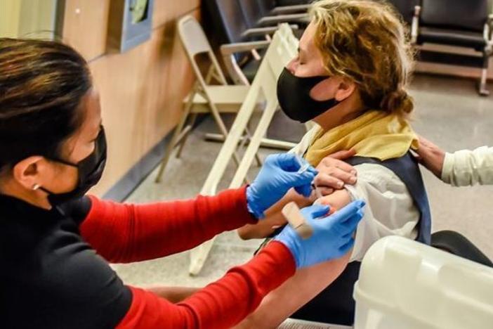 Margaret Applegate (in yellow scarf), a United Airlines customer service agent, is accompanied by Lori Augustine, vice president of United's San Francisco hub, as Applegate gets a COVID-19 vaccine in September ahead of United's mandated deadline.