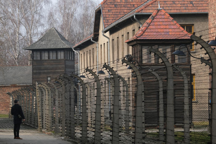 A visitor walks near barbed wire and prison barracks at the former Auschwitz I concentration camp on Jan. 26, 2020, in Oswiecim, Poland.