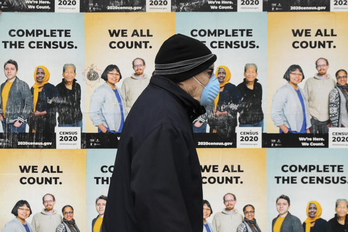 A person wearing a mask walks past posters encouraging census participation in Seattle in April 2020. The coronavirus pandemic has disrupted not only last year's national head count, but also a critical follow-up survey that the U.S. Census Bureau relies on to determine the tally's accuracy.