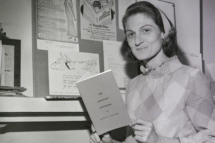 Patricia Maginnis holds her <em>Abortees' Songbook</em> and stands next to a bulletin board full of abortion information. The early abortion rights advocate, pictured here in 1970, died earlier this year.