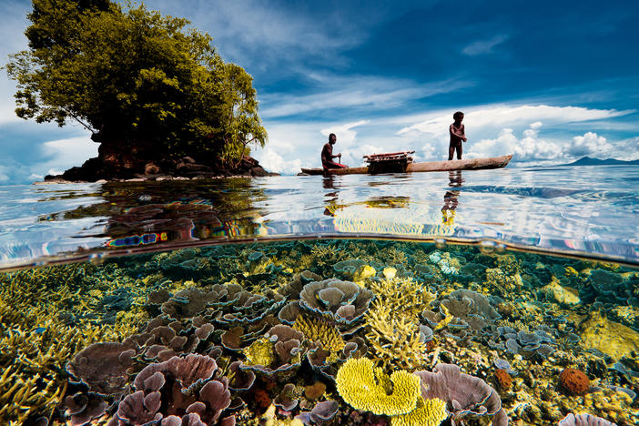 A fisherman sails with his son in an outrigger. They live in a village on the Willaumez Peninsula on New Britain Island, Kimbe Bay, Papua New Guinea.