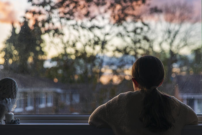 A girl looks out of her bedroom window as the sun is setting.