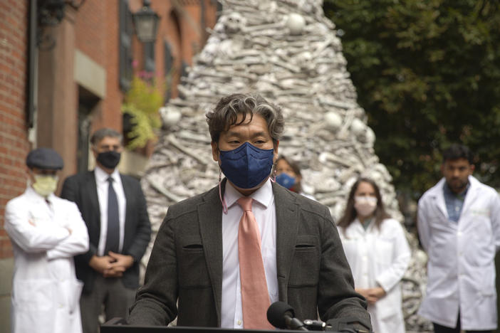 Dr. KJ Seung, a professor at Harvard Medical School, speaks at a September rally outside the home of the CEO of Moderna, maker of one of the two mRNA vaccines that prevent COVID-19. The fake bones are meant to represent lives lost unnecessarily to the coronavirus. Seung was part of a group of doctors demanding Moderna share vaccines — and its recipe — with low-resource countries.