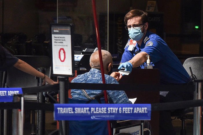 A man using a wheelchair hands his ID to an officer at a security screening checkpoint at Orlando International Airport in 2020.