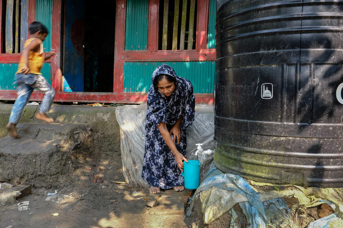 Sitara Begum fills buckets with drinking water from a plastic water tank.