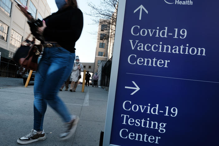 People walk by a sign for both a COVID-19 testing clinic and a Covid vaccination location outside of a Brooklyn, New York, hospital on March, 29 2021.