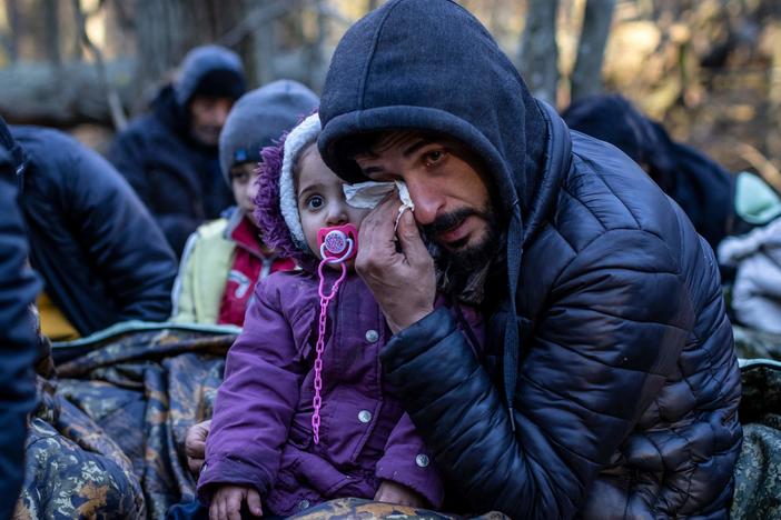 A man holding a child wipes his eye as the Kurdish family from Dohuk in Iraq waits for the border guard patrol, near Narewka, Poland, near the Polish-Belarusian border on Nov. 9. The three-generation family of 16 — with seven minors, including the youngest who is 5 months old — spent about 20 days in the forest and was pushed back to Belarus eight times.