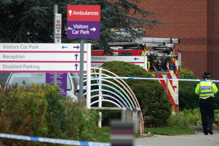 A police officer walks past a fire engine at Liverpool Women's Hospital in Liverpool, England, on Monday. One person died and another was injured after a device exploded in a taxi outside the hospital on Sunday.