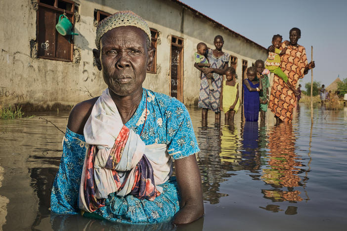 Nyayua Thang, 62, left, stands waist-deep in the floodwaters in front of an abandoned primary school in South Sudan. Members of her village, displaced by extreme flooding as a result of heavy rainfall, are using the building as a refuge. Only small mud dikes at the entrance of the door are keeping the water out. (November 2020)