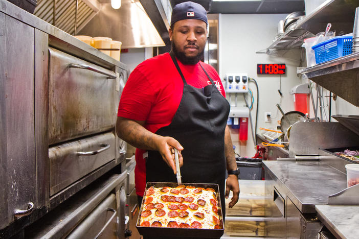 Down North Pizza employee Myles Jackson presents a pie from the oven.