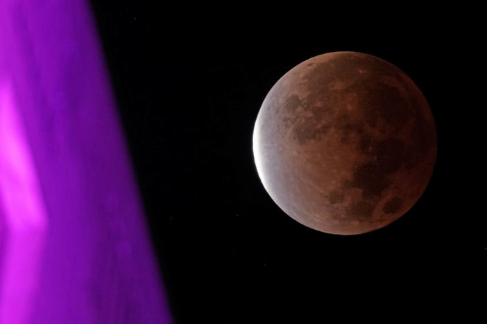 The earth's shadow covers the full moon during a partial lunar eclipse as it sets beyond city hall, Friday, Nov. 19, in downtown Kansas City, Mo.
