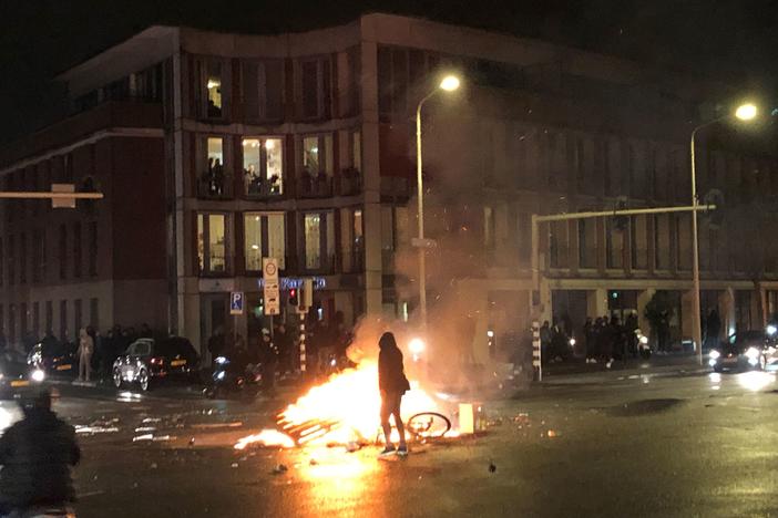 A man walks in front of a fire in a street of The Hague during a demonstration against the Dutch government's coronavirus measures on November 20, 2021.