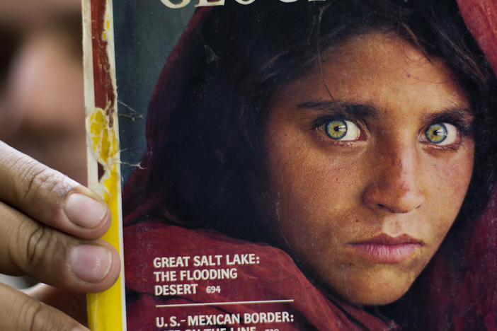In this file photo from 2016, a bookshop owner in Pakistan shows a National Geographic magazine with the cover photograph of Afghan refugee woman Sharbat Gula. She arrived in Italy as part of the West's evacuation of Afghans following the Taliban takeover of the country, the Italian government said Thursday. The office of Premier Mario Draghi said she asked to be helped to leave the country.