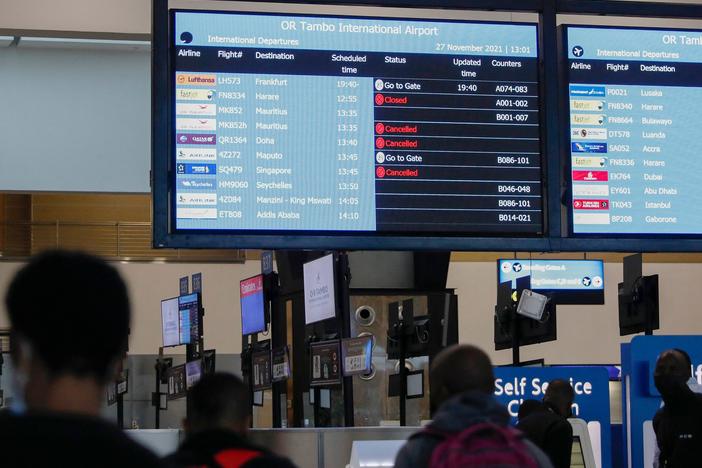 Travelers walk near an electronic flight notice board displaying canceled flights at O.R. Tambo International Airport in Johannesburg, South Africa, on Saturday. Several countries have begun travel bans in response to the omicron variant.