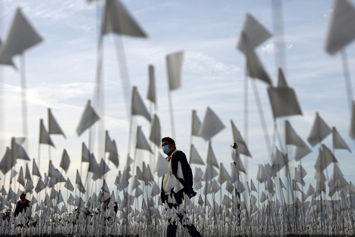 A person wearing a face covering walks past a white flag memorial installation outside Griffith Observatory honoring the nearly 27,000 Los Angeles County residents who have died from COVID-19 on Nov. 18 in Los Angeles, Calif.