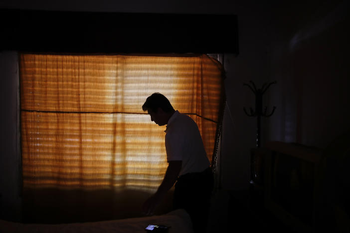 Claudio Rojas, who was deported from the U.S. in 2019, is silhouetted against a curtained window of his home in Moreno, Argentina, on May 8, 2021. He was able to return to the U.S. in August.