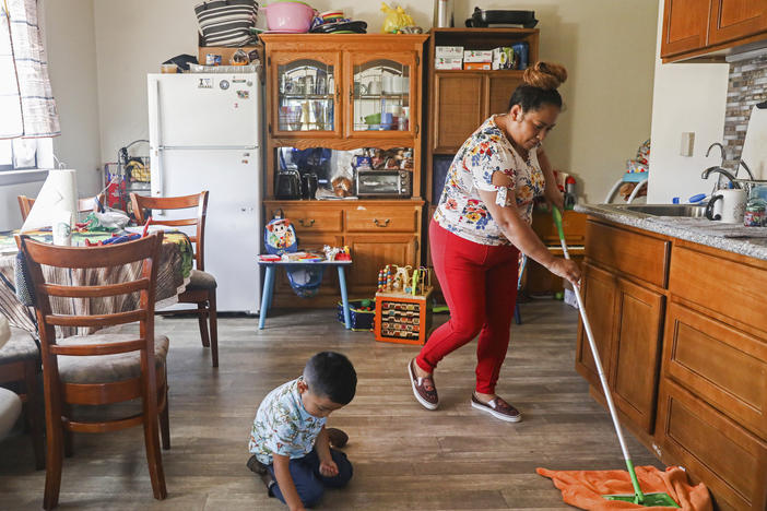 Mirna Arana mops the floor after playing with her son in her home in Oakland, Calif., Oct. 25, 2021. Arana works as a housecleaner in San Francisco and is hopeful about a proposed law that would give domestic workers paid sick leave.