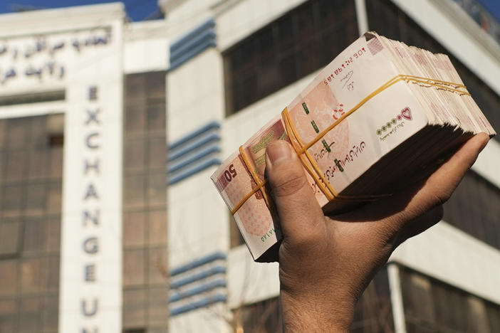 An Afghan money changer holds a stack of Iranian currency at Khorasan market in Herat, Afghanistan, The value of Afghanistan's currency is tumbling, exacerbating an already severe economic crisis.
