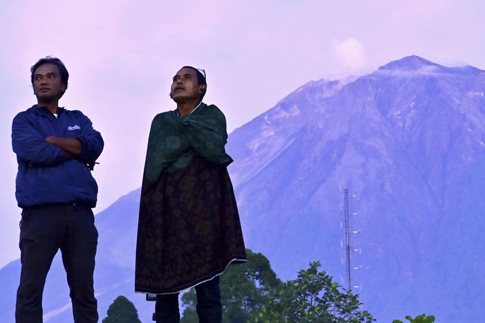 Indonesian villagers stand with Mount Semeru in the background on Saturday. Indonesian authorities raised the alert level for the highest volcano on Java island, saying it could blow up again after a sudden eruption earlier this month that killed dozens of people and left thousands homeless in villages that were buried in layers of mud.