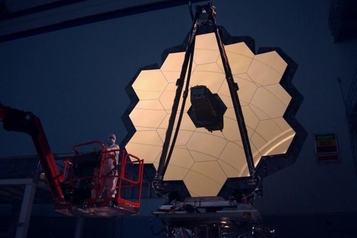 The James Webb Space Telescope's primary mirror is illuminated inside a darkened clean room. The entire telescope is now packed inside a rocket, awaiting launch.