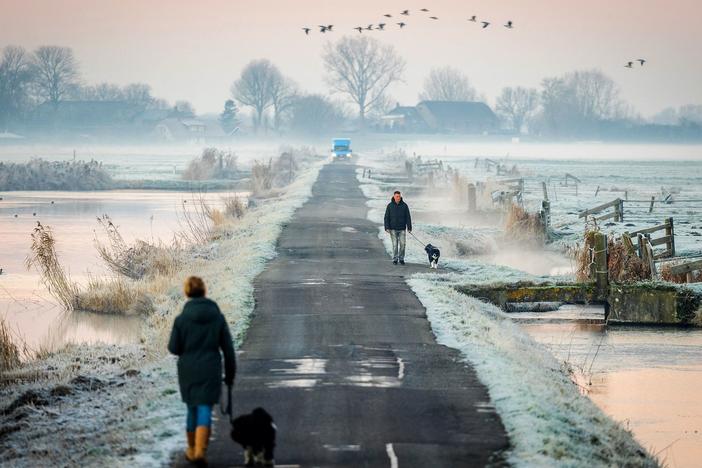 People walk their dogs along a narrow road as the first winter frost blankets the fields in Oudeland van Strijen in the Netherlands on Tuesday. It's the shortest day of the year and official start of winter.