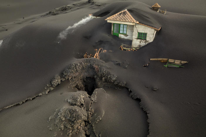A fissure is seen next to a house covered with ash on the Canary island of La Palma on  Dec. 1. Authorities on the Spanish island are declaring a volcanic eruption that has caused widespread damage but no casualties officially finished.