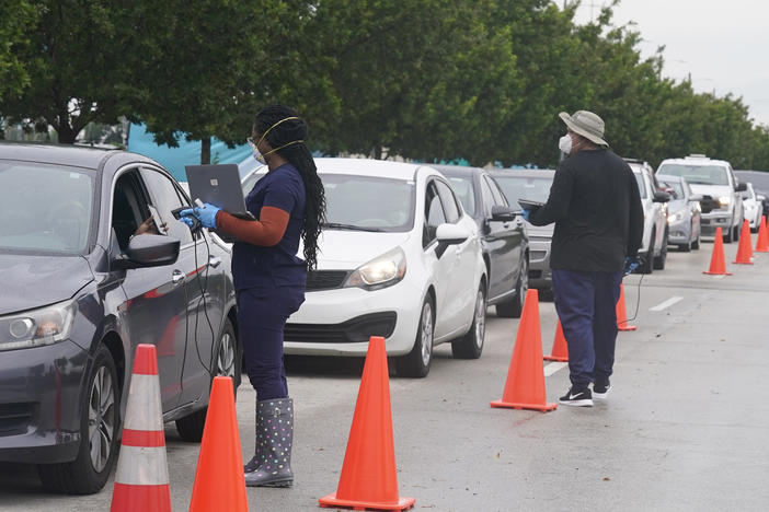 Employees of Nomi Health check in a long line of people for COVID-19 tests on Tuesday in North Miami, Fla.