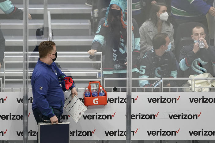 Seattle Kraken fan Nadia Popovici (center) looks toward Vancouver Canucks assistant equipment manager Brian "Red" Hamilton (left) at the end of an NHL hockey game in Seattle on Saturday. Popovici had written Hamilton a note months earlier urging him to see a doctor about a suspicious mole, which turned out to be cancerous.