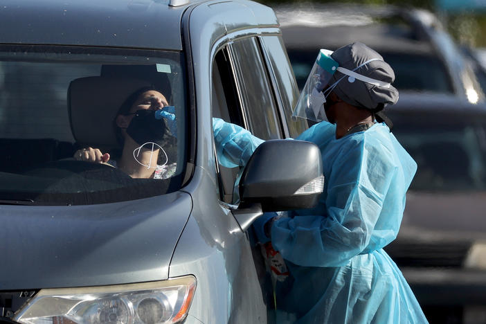A health care worker conducts a test at a drive-through COVID-19 testing site at Zoo Miami last Wednesday in Miami. In response to the increasing demand for COVID-19 tests, Miami-Dade County opened two new testing sites and expanded hours at the Zoo Miami testing location.