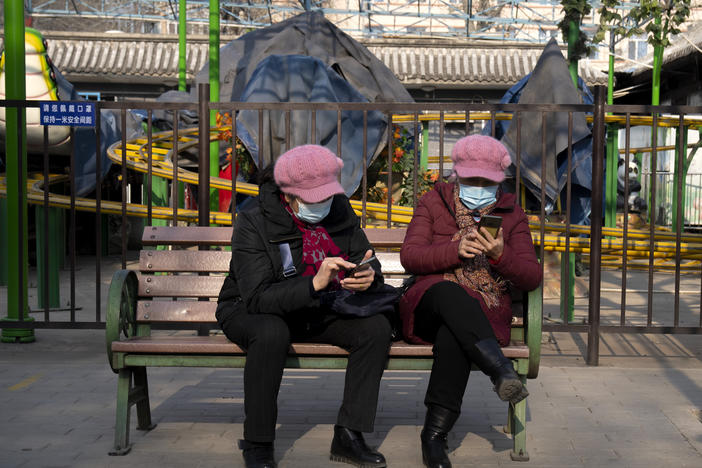 Women wearing face masks to protect against COVID-19 look at their smartphones at a public park in Beijing Wednesday. China is reporting a major drop in local COVID-19 infections in the northern city of Xi'an, which has been under a tight lockdown for the past two weeks.