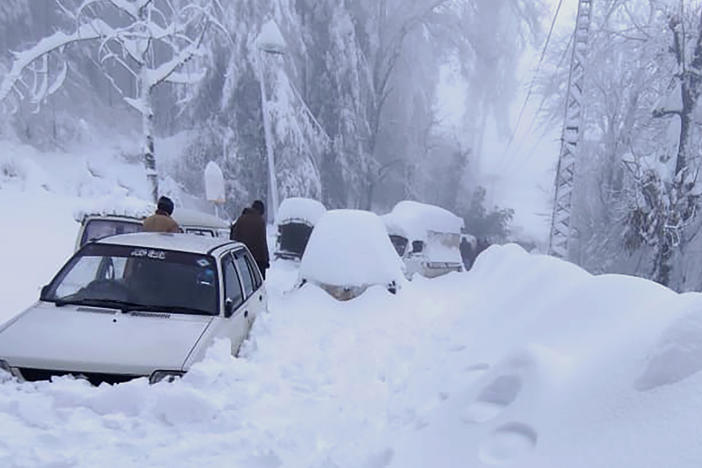 People walk past vehicles trapped in a heavy snowfall-hit area in Murree, some 28 miles north of the capital of Islamabad, Pakistan, on Saturday.