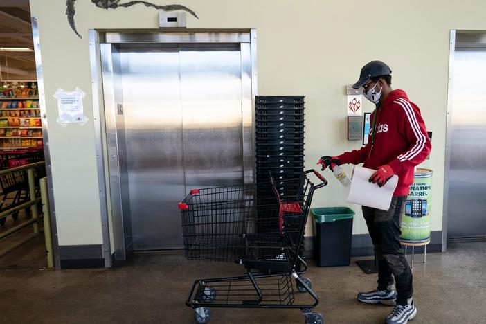 A grocery store worker sanitizes a shopping cart at a MOM's Organic Market in Washington, D.C., in April 2020.