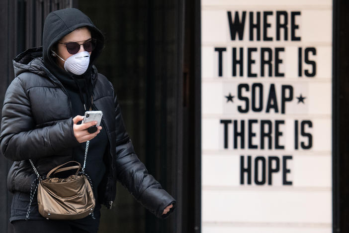 A woman wearing a protective mask walks past a sign in a cosmetic shop window on March 17, 2020 in London, England.