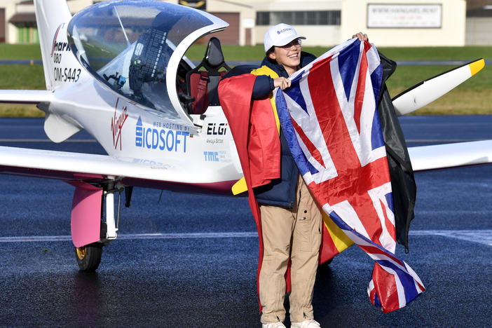 Zara Rutherford, 19, carries the Belgian and British flags on the tarmac after landing her Shark ultralight plane at the Kortrijk airport in Belgium, on Thursday at the completion of a record-breaking solo circumnavigation.